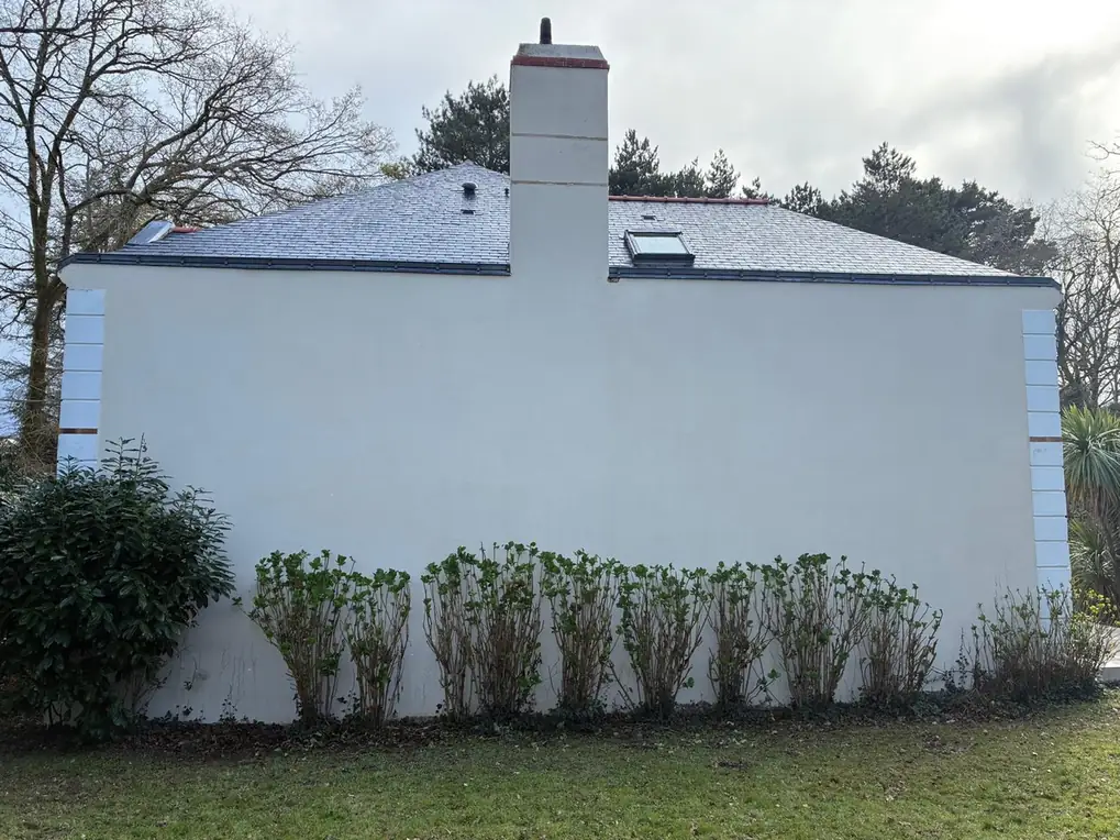 Maison claire derrière une haie taillée, pignon dégagé
