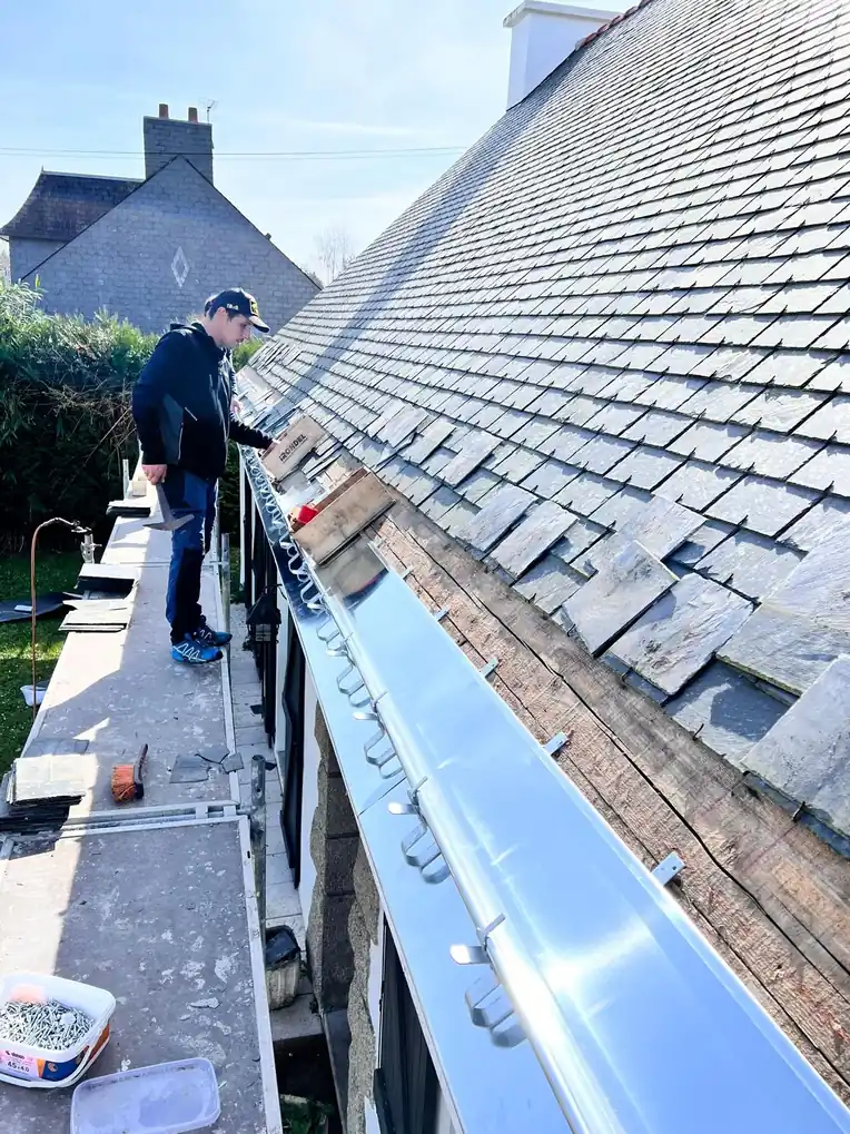 Couvreur travaillant sur une toiture en ardoise, gouttière neuve posée